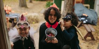 Three children in Halloween costumes joyfully trick-or-treating with candy buckets.