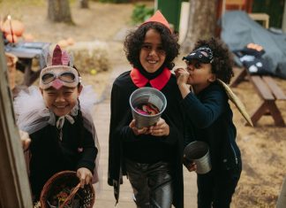 Three children in Halloween costumes joyfully trick-or-treating with candy buckets.