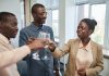 Three adults celebrate with a toast indoors, expressing joy and camaraderie.