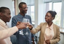 Three adults celebrate with a toast indoors, expressing joy and camaraderie.