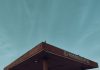 A lone bird perches on a weathered gas station canopy against a serene sky.
