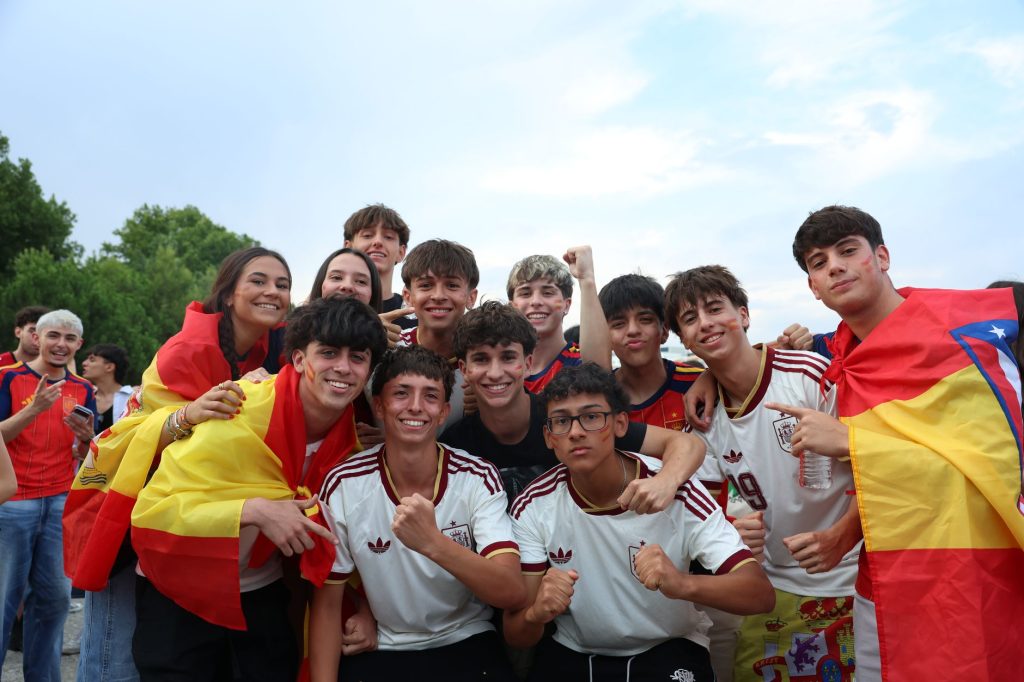 A cheerful group of young people celebrates outdoors, proudly displaying Spanish flags and team jerseys.