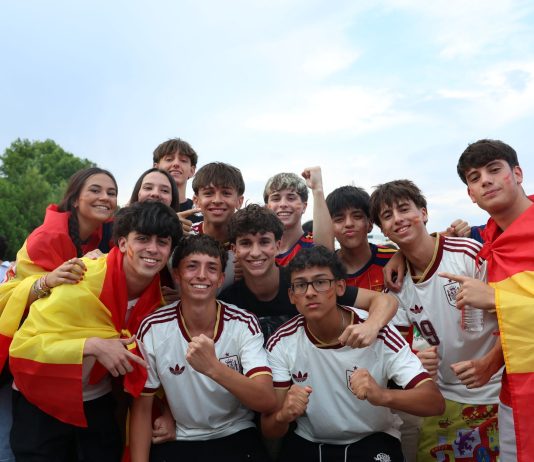 A cheerful group of young people celebrates outdoors, proudly displaying Spanish flags and team jerseys.