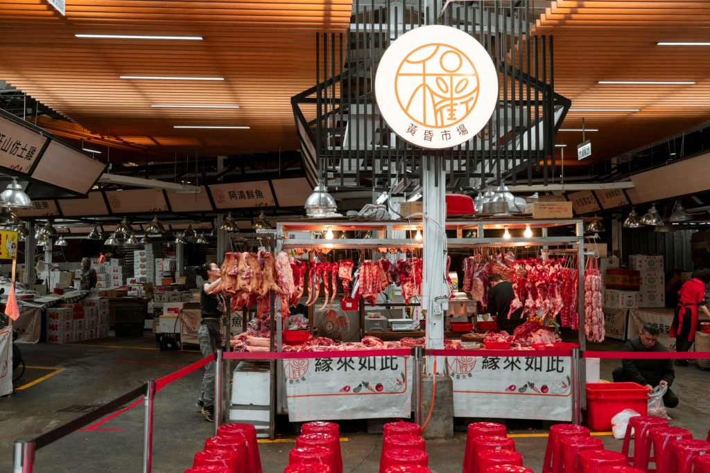 Active Asian market scene showcasing an indoor butcher stall with various meat cuts and vibrant red seating.