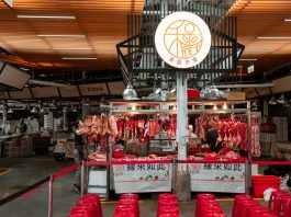 Active Asian market scene showcasing an indoor butcher stall with various meat cuts and vibrant red seating.