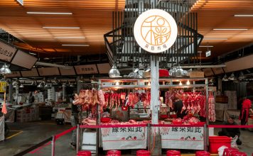 Active Asian market scene showcasing an indoor butcher stall with various meat cuts and vibrant red seating.