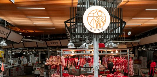 Active Asian market scene showcasing an indoor butcher stall with various meat cuts and vibrant red seating.