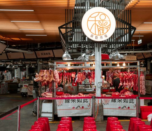 Active Asian market scene showcasing an indoor butcher stall with various meat cuts and vibrant red seating.
