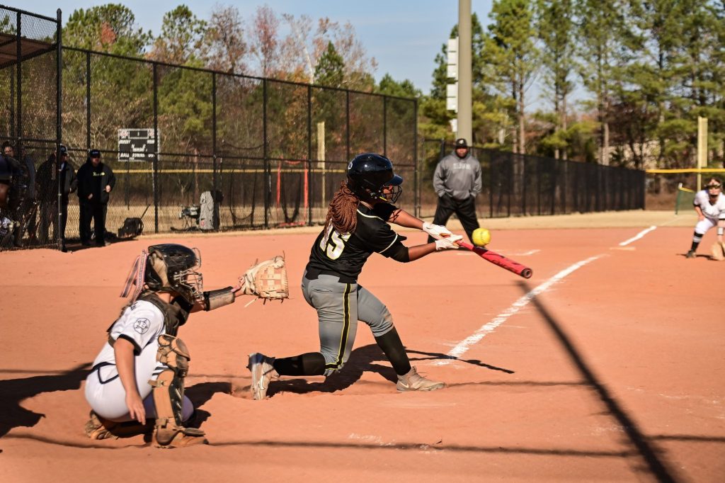 A dynamic moment during a women's softball game with the batter hitting the ball.