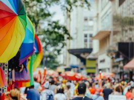 Colorful rainbow umbrellas adorn a lively outdoor city festival with a bustling crowd.