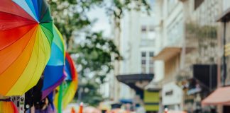 Colorful rainbow umbrellas adorn a lively outdoor city festival with a bustling crowd.