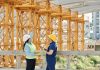 Two engineers in hardhats discuss projects at a busy construction site.
