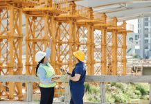 Two engineers in hardhats discuss projects at a busy construction site.