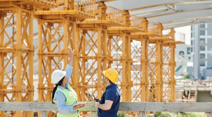 Two engineers in hardhats discuss projects at a busy construction site.