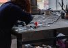Redhead artisan working meticulously on stained glass artwork at a workshop table.