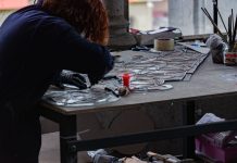 ÚLTIMA HORA: Nuevo estudio de vitrales abre en Jersey City Redhead artisan working meticulously on stained glass artwork at a workshop table.