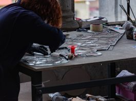 Redhead artisan working meticulously on stained glass artwork at a workshop table.