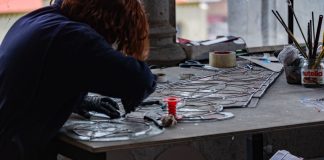 Redhead artisan working meticulously on stained glass artwork at a workshop table.