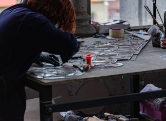 Redhead artisan working meticulously on stained glass artwork at a workshop table.