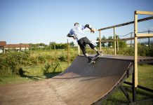 Skateboarder executing a trick on a wooden outdoor skate ramp with lush greenery in the background.