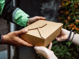 Close-up of a delivery person handing over a box to a customer outdoors.