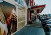Outdoor view of fashion stores and advertising poster with parked cars and pedestrians.