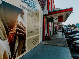Outdoor view of fashion stores and advertising poster with parked cars and pedestrians.