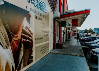 Outdoor view of fashion stores and advertising poster with parked cars and pedestrians.