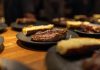 Close-up of a succulent grilled steak served indoors with roasted sides on black plates.