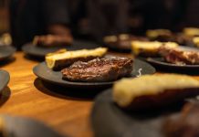 Close-up of a succulent grilled steak served indoors with roasted sides on black plates.