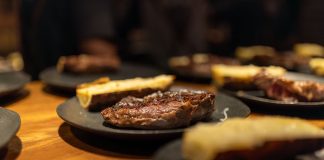 Close-up of a succulent grilled steak served indoors with roasted sides on black plates.