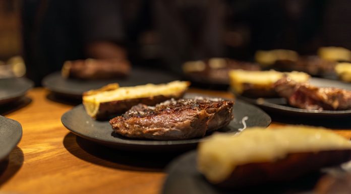 Close-up of a succulent grilled steak served indoors with roasted sides on black plates.
