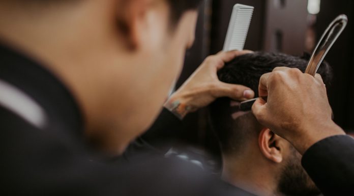 Close-up of a barber expertly styling a man's hair with a razor and comb in a trendy barbershop.