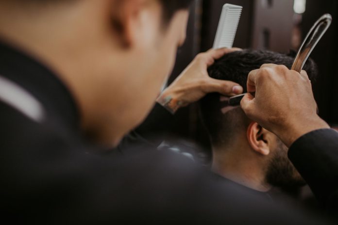 mejores-barberias-salones-union-city Close-up of a barber expertly styling a man's hair with a razor and comb in a trendy barbershop.