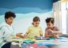 Children focusing on an art project with colored papers in a playful art class setting.
