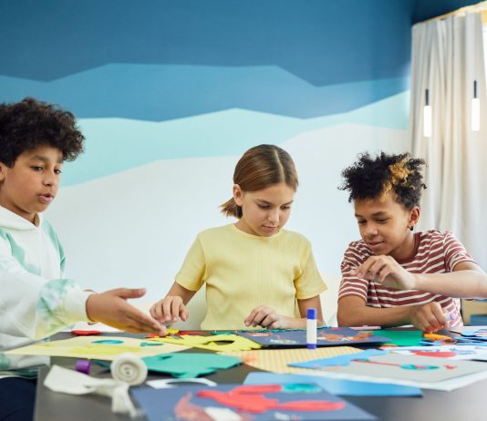 Children focusing on an art project with colored papers in a playful art class setting.