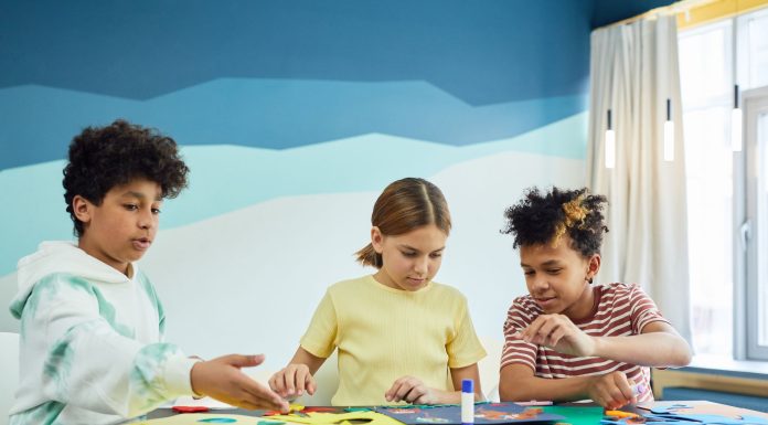 Children focusing on an art project with colored papers in a playful art class setting.