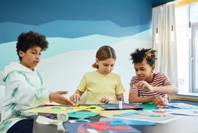 Children focusing on an art project with colored papers in a playful art class setting.