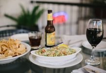 An inviting dining setup featuring tacos, chips, beer, and wine on a glass table in a relaxed indoor setting.
