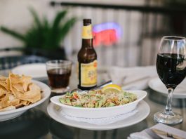 An inviting dining setup featuring tacos, chips, beer, and wine on a glass table in a relaxed indoor setting.
