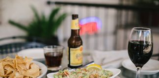An inviting dining setup featuring tacos, chips, beer, and wine on a glass table in a relaxed indoor setting.