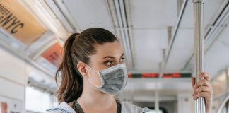 An adult woman wearing a face mask rides public transportation, focusing on safety and protection.
