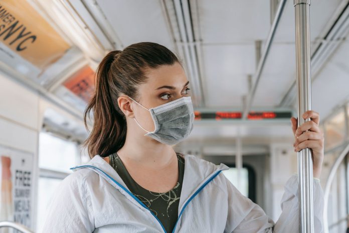 An adult woman wearing a face mask rides public transportation, focusing on safety and protection.