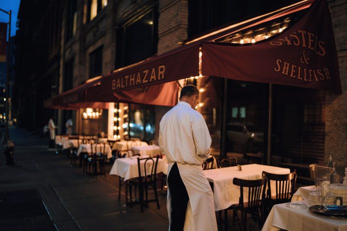 restaurantes-abiertos-hasta-tarde-bayonne-2026 Elegant outdoor dining area at night with waitstaff preparing tables.