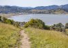 Peaceful path through grassy hills with a serene lake view on a sunny day.