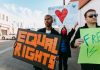 A diverse group of protesters holding signs advocating for equal rights and world peace.