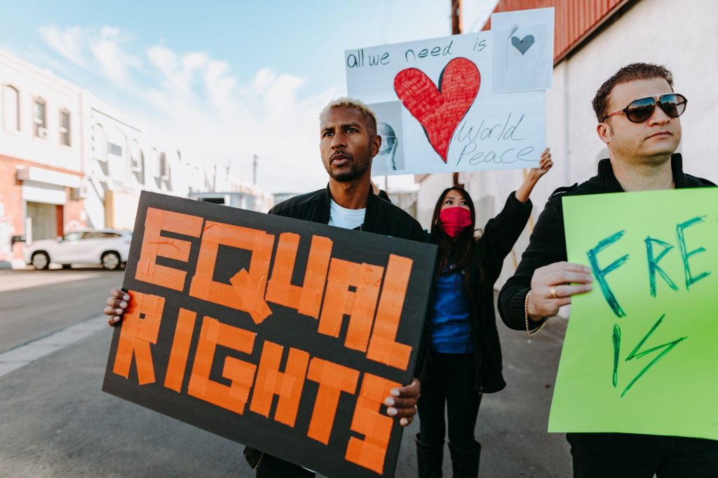 A diverse group of protesters holding signs advocating for equal rights and world peace.