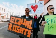 A diverse group of protesters holding signs advocating for equal rights and world peace.