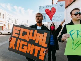 A diverse group of protesters holding signs advocating for equal rights and world peace.
