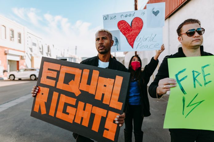 A diverse group of protesters holding signs advocating for equal rights and world peace.
